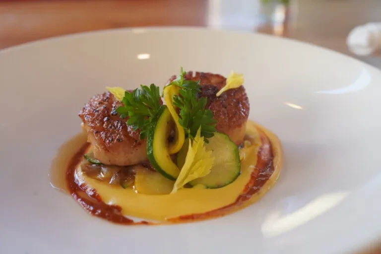 Two seared scallops on creamy yellow purée, green garnish, white plate.
