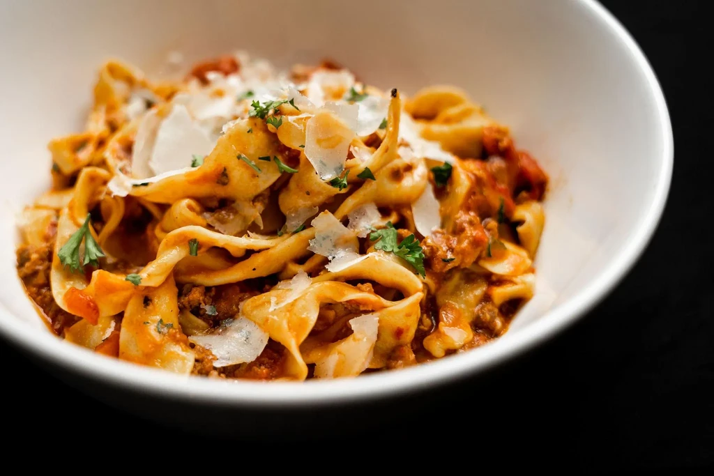 Close-up of pasta with meat sauce, grated cheese, and herbs.