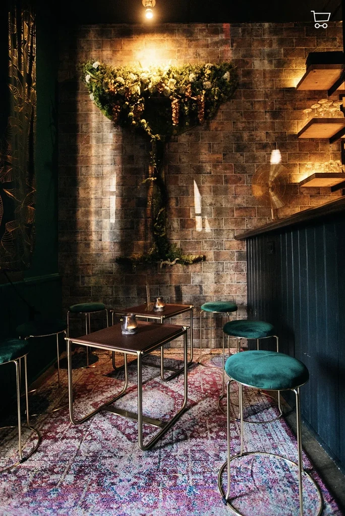 Moody bar interior with brick wall, velvet stools, and large floral display.