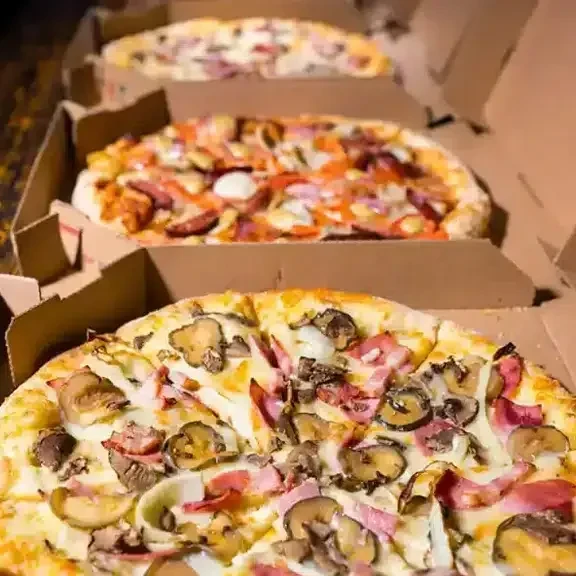 Three assorted pizzas in open delivery boxes, close-up view.