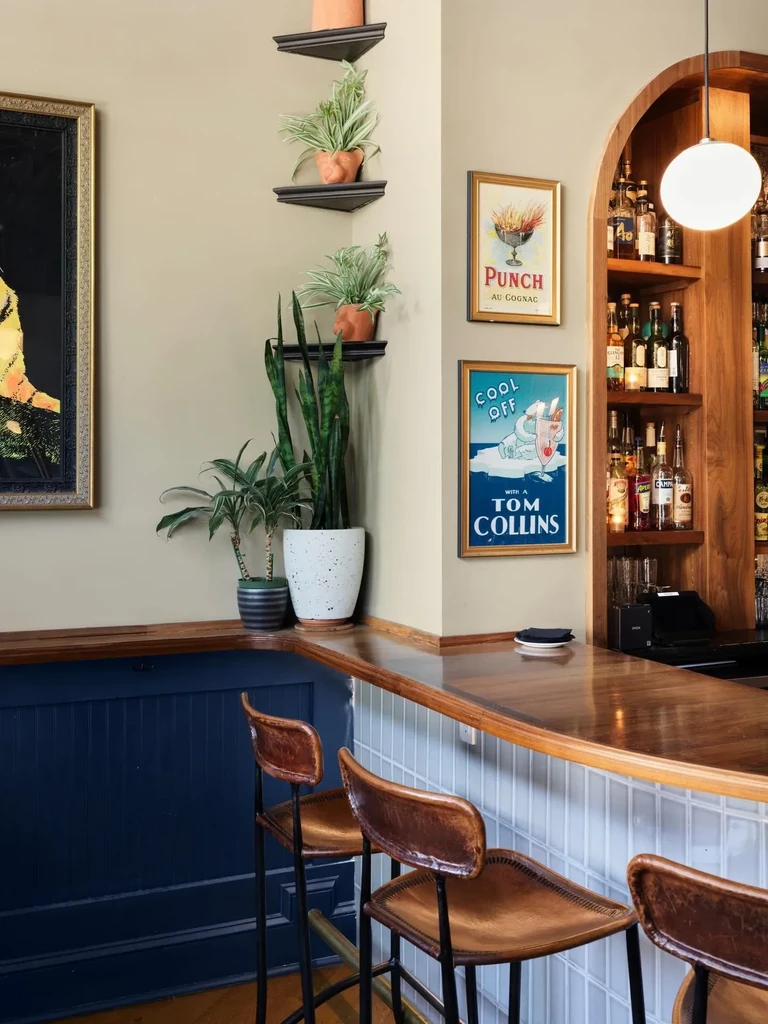 Bar corner: wood counter, leather stools, plants, liquor, and vintage ads.