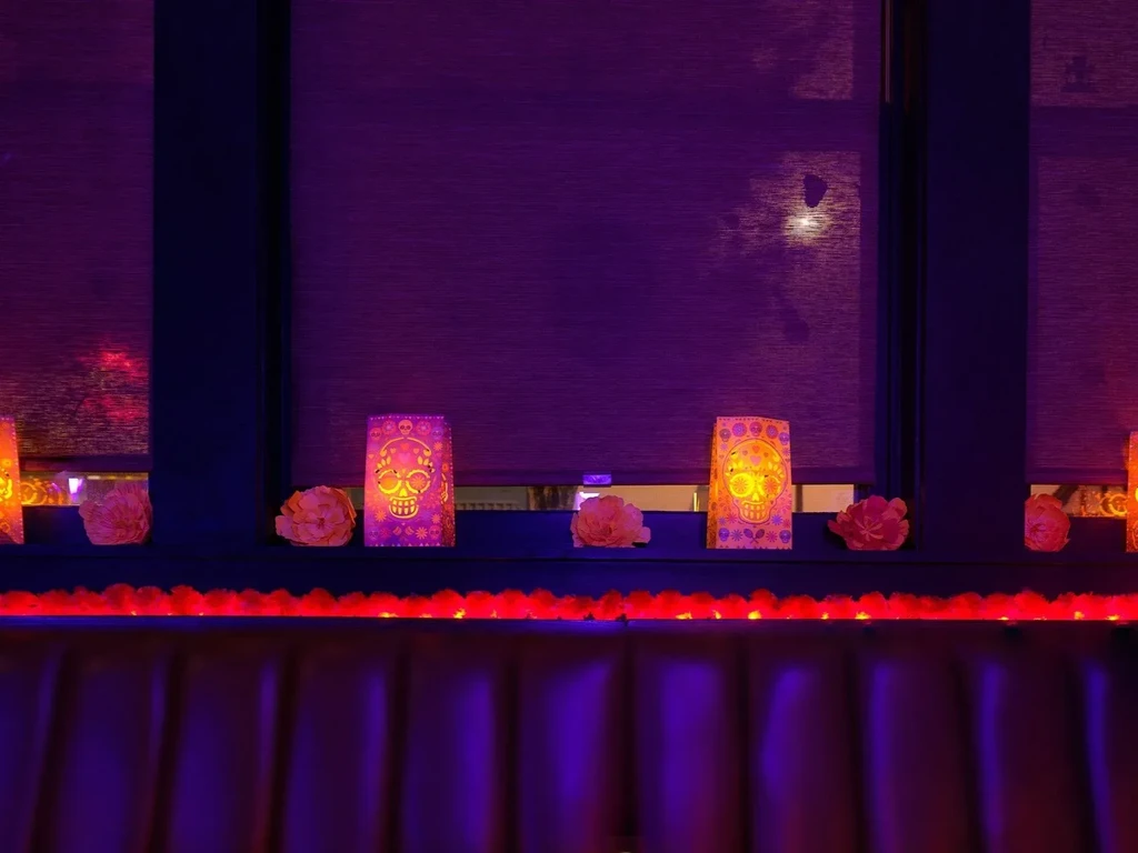 Decorated window sill with glowing sugar skulls, flowers, and purple-red lighting.
