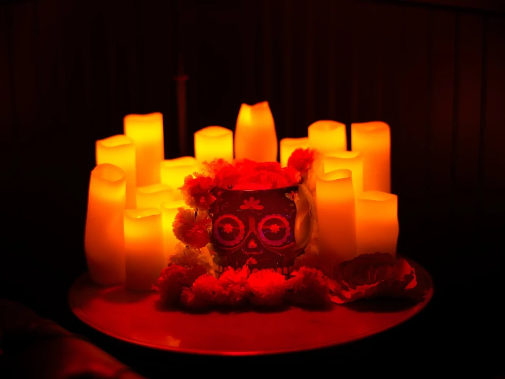 Calavera mug with red flowers amidst glowing pillar candles.