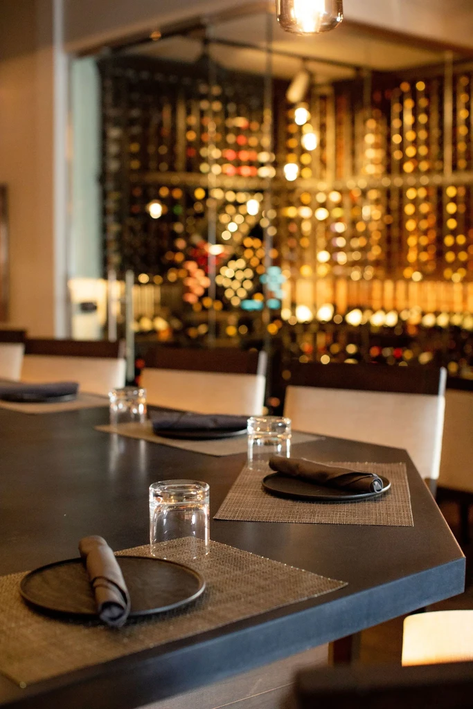 Elegant dining table with settings, a blurred wine cellar backdrop.