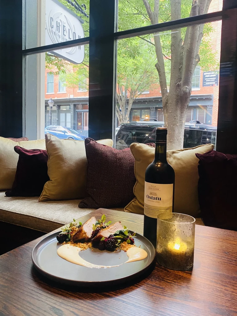 Plated roasted meat, Ostatu Crianza wine, and candle overlooking city.