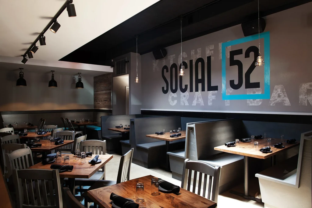 Modern restaurant dining area with tables, booths, and "SOCIAL 52" wall art.