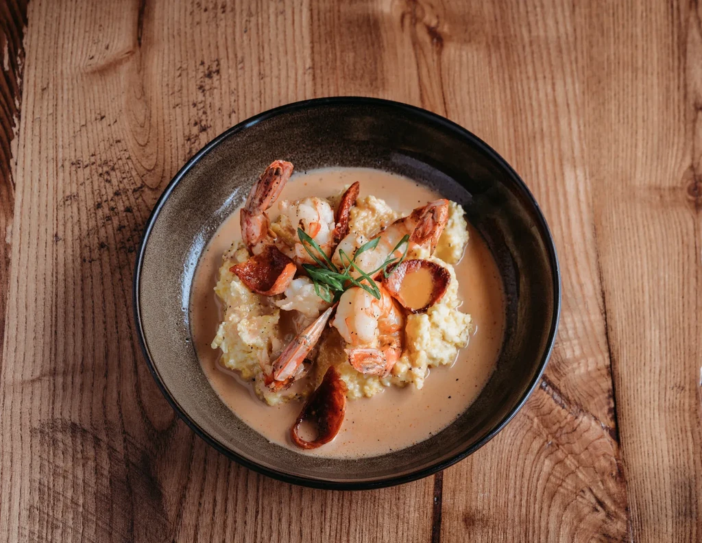 Top-down view of shrimp and grits with chorizo, sauce, and green herbs.