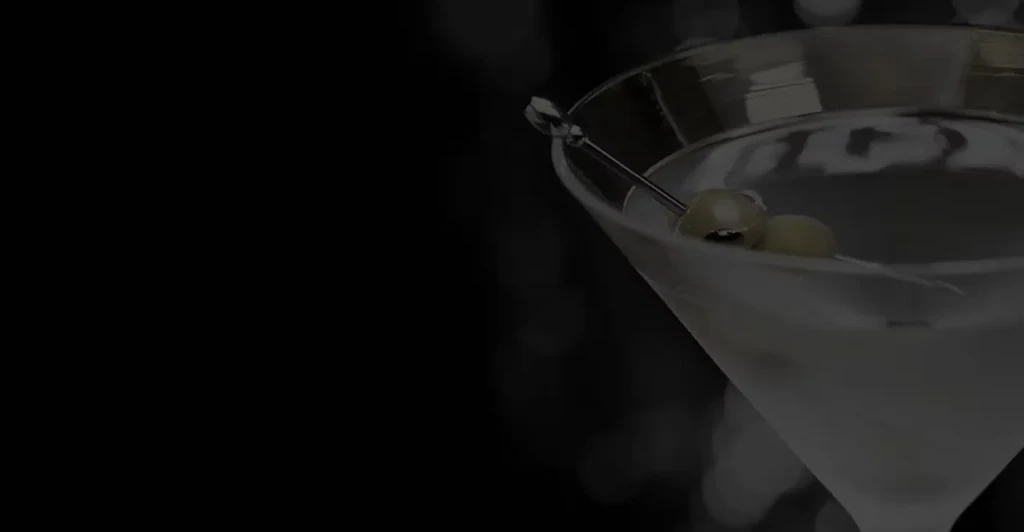 Close-up of a clear martini with green olives in a dark bar.