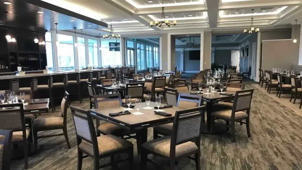 Spacious, empty restaurant with dining tables, bar, and large windows.