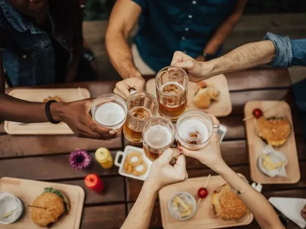 Diverse hands clinking beer glasses above burgers, fries on table.