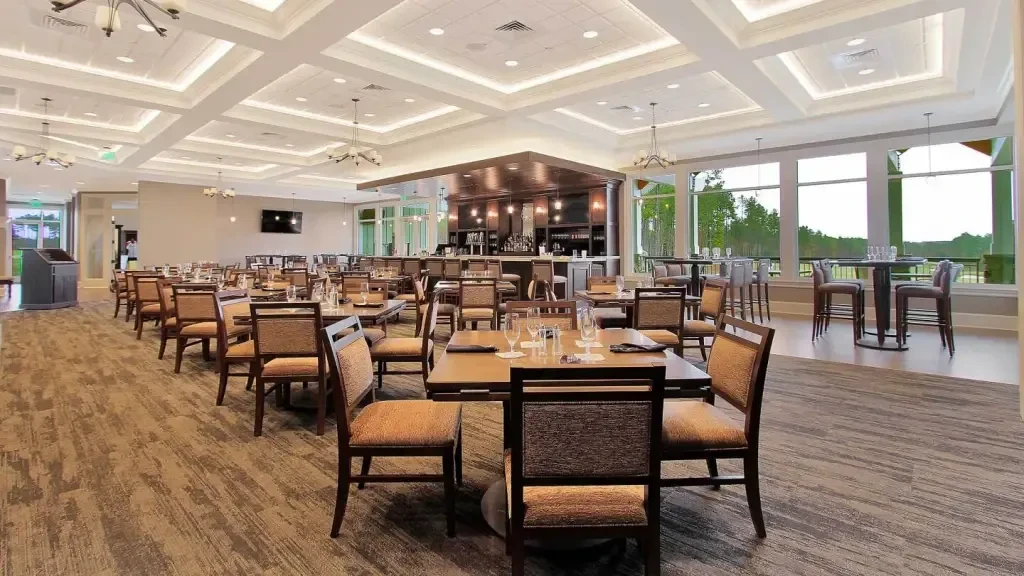 Modern spacious restaurant interior with dining area, prominent bar, and green view.