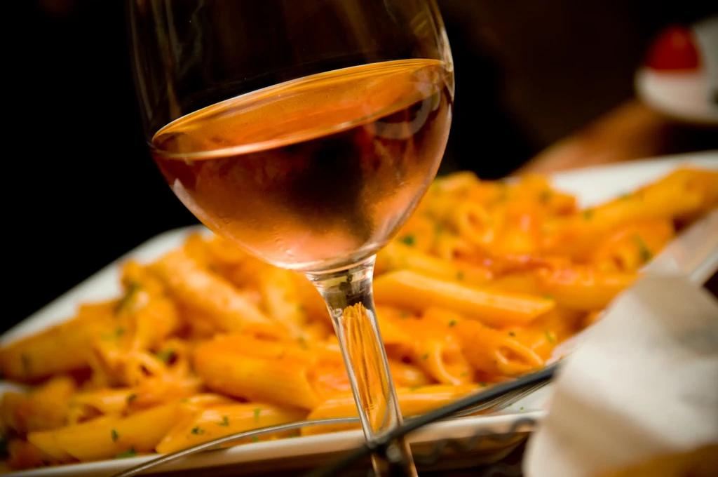 Wine glass with amber liquid, blurred pasta dish in restaurant.