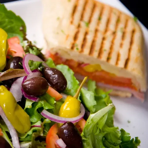 Fresh salad with olives and tomatoes next to a grilled panini.
