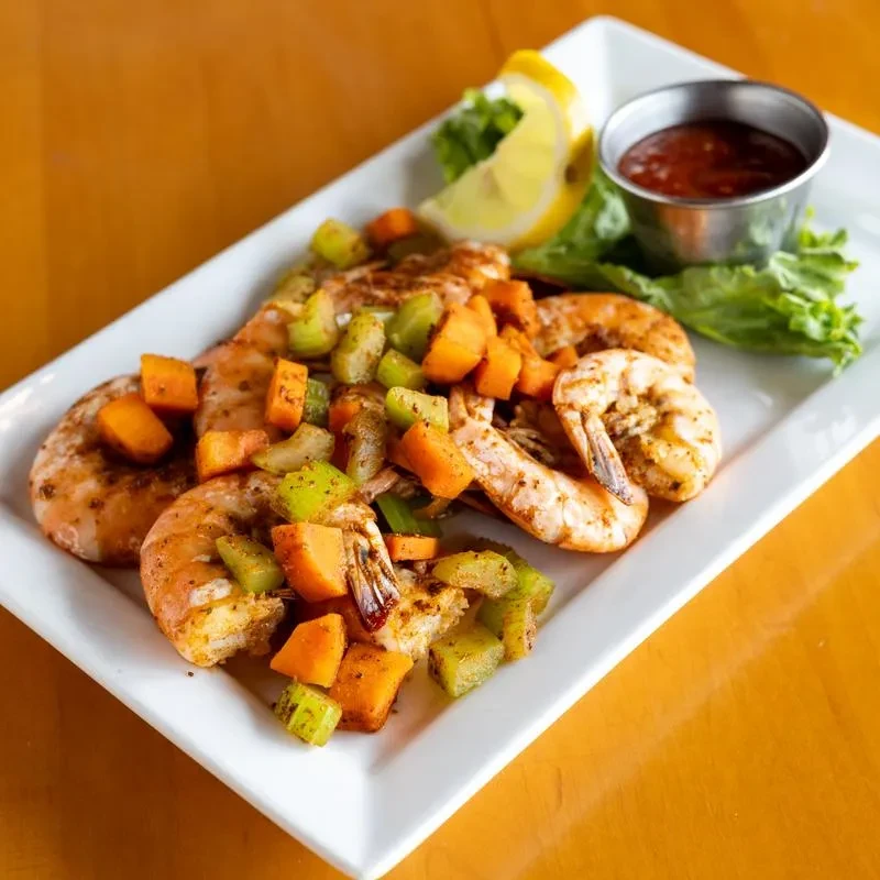 Seasoned shrimp with diced vegetables, lemon, and sauce on a white plate.