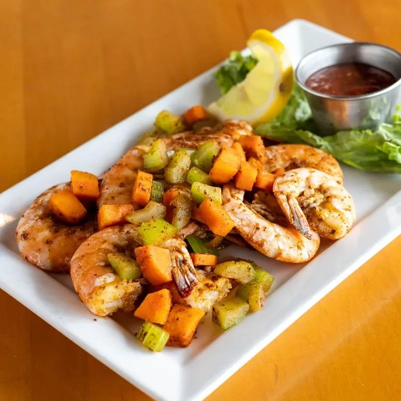 Plated shrimp with colorful diced vegetables, a red dipping sauce, and lemon.