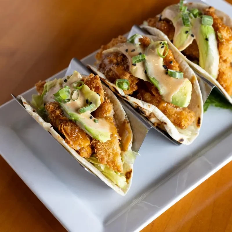 Three crispy fried tacos with sauce, avocado, and green onions.
