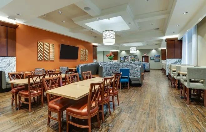 Empty modern dining room with varied seating and an orange accent wall.