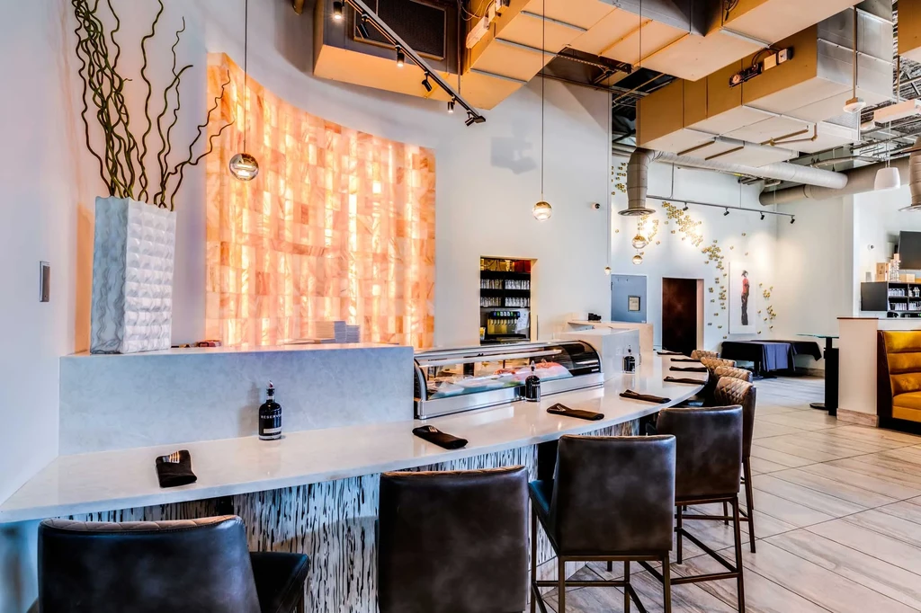 Modern sushi bar, white counter, glowing orange stone backdrop.