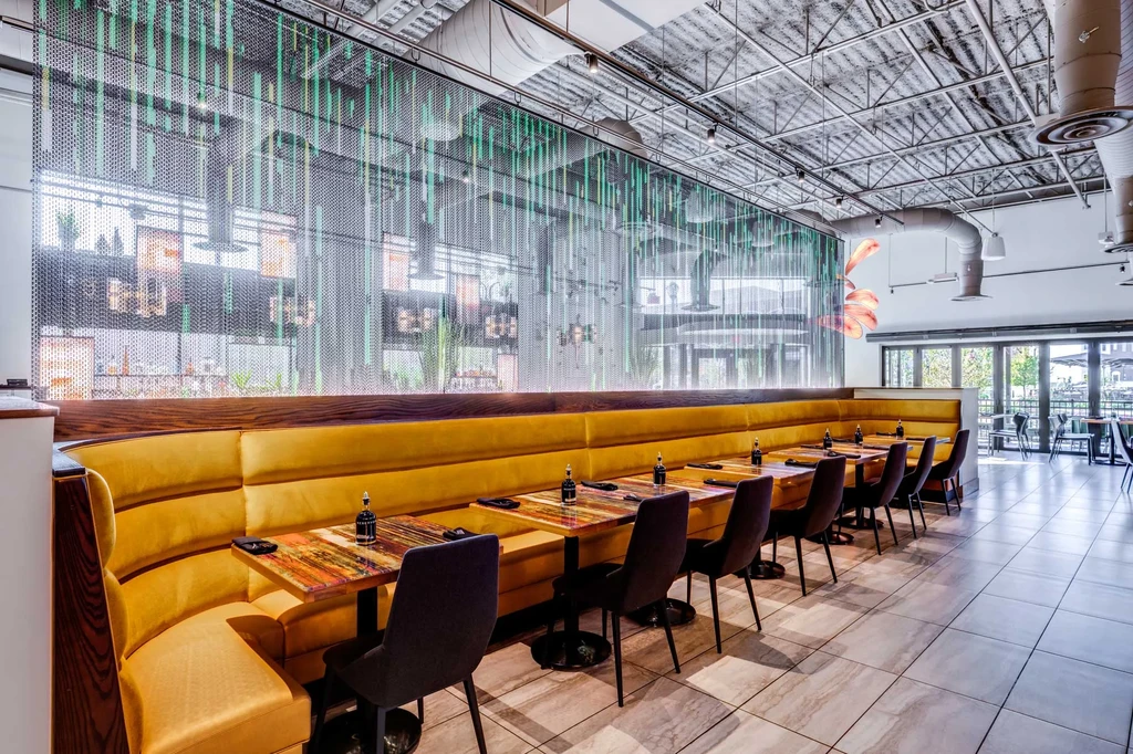 Empty modern restaurant: mustard yellow booth, colorful tables, green screen.