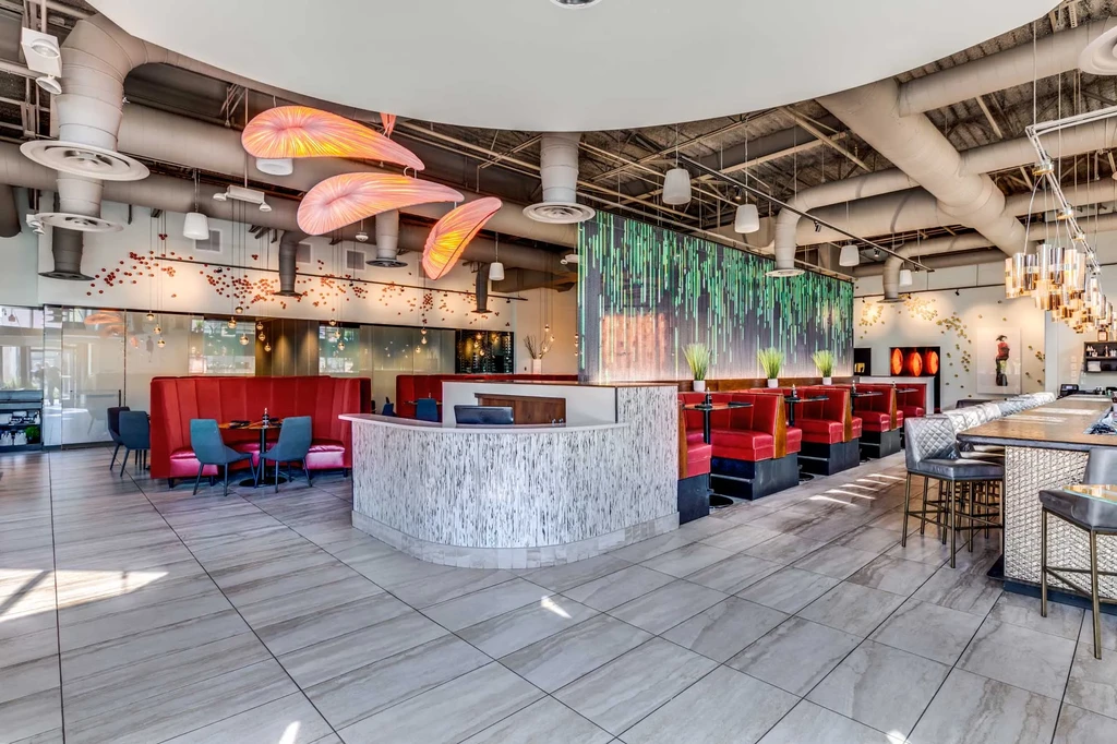 Empty modern restaurant interior with red booths, striped wall, and bar.