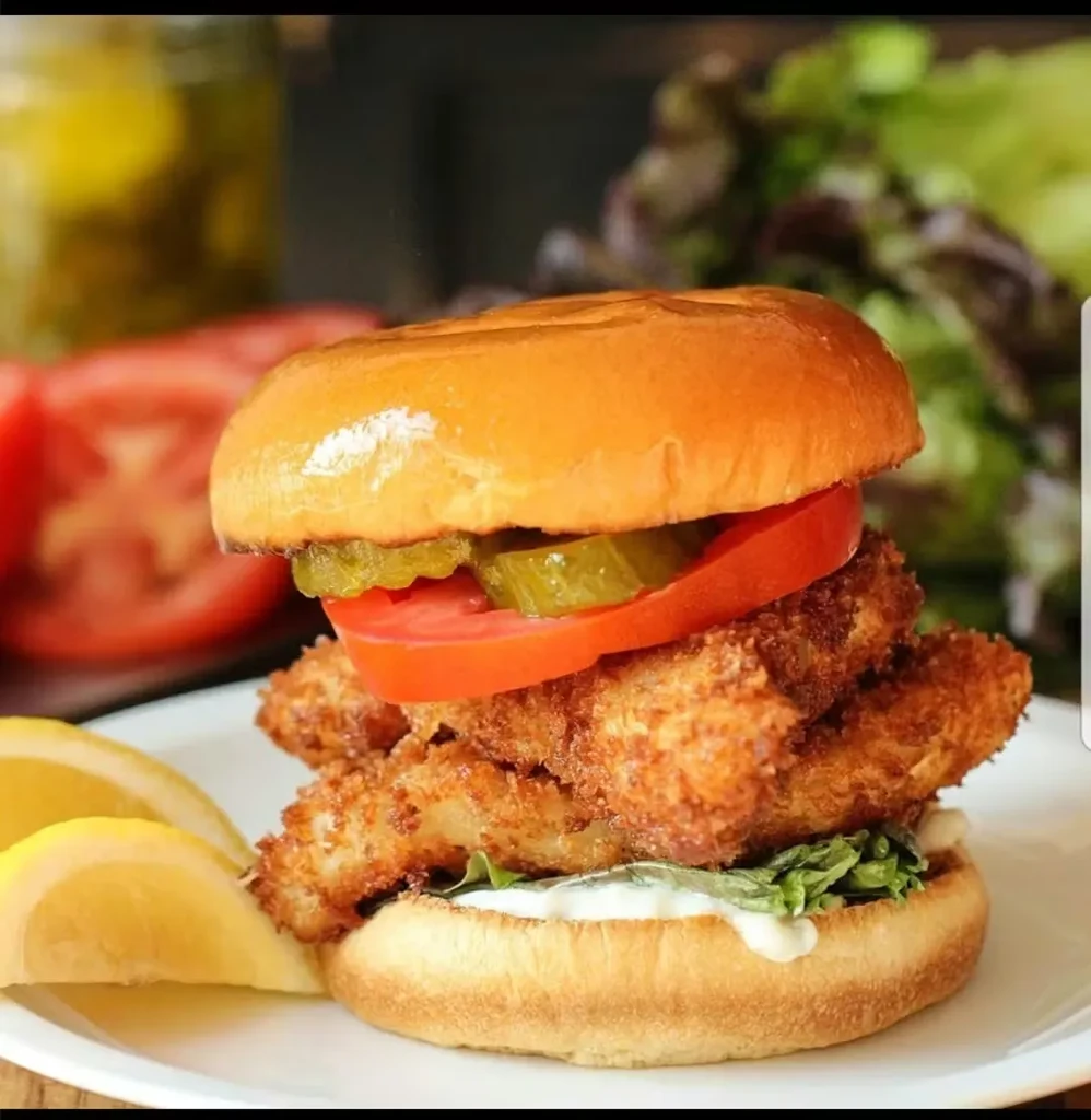 Crispy chicken sandwich with lettuce, tomato, pickles, and lemon wedges.