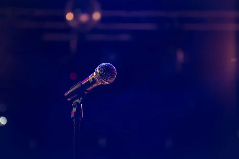 Close-up of a microphone on stand with colorful, blurred stage lights.