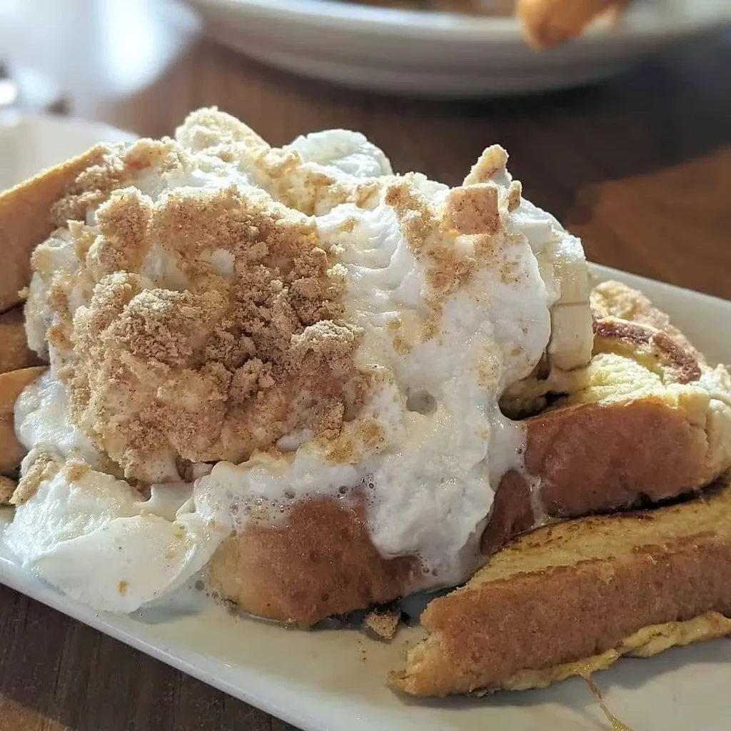 Thick French toast, whipped cream, banana, and crumbs on a white plate.