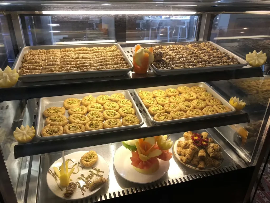 Clear display case with Middle Eastern baklava, pistachio pastries, and plated desserts.