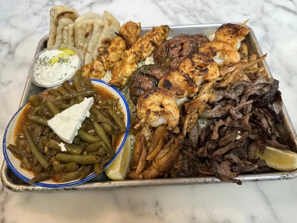 Large platter of grilled Mediterranean meats, rice, green beans, and pita.