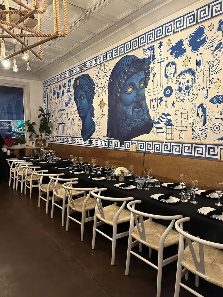 Warm restaurant interior featuring a set table and classical-style wall mural.