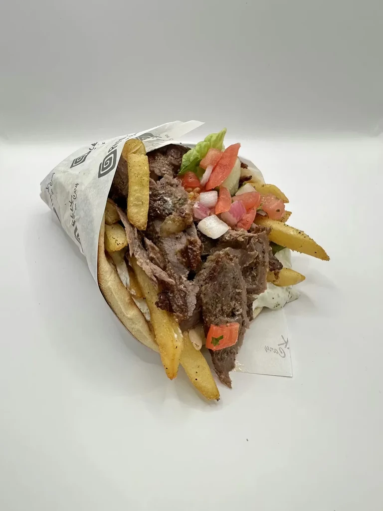 A pita gyro overflowing with meat, french fries, and vegetables.
