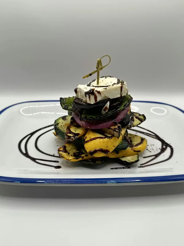 Stacked grilled vegetables, white cheese, balsamic glaze, and wooden skewer.