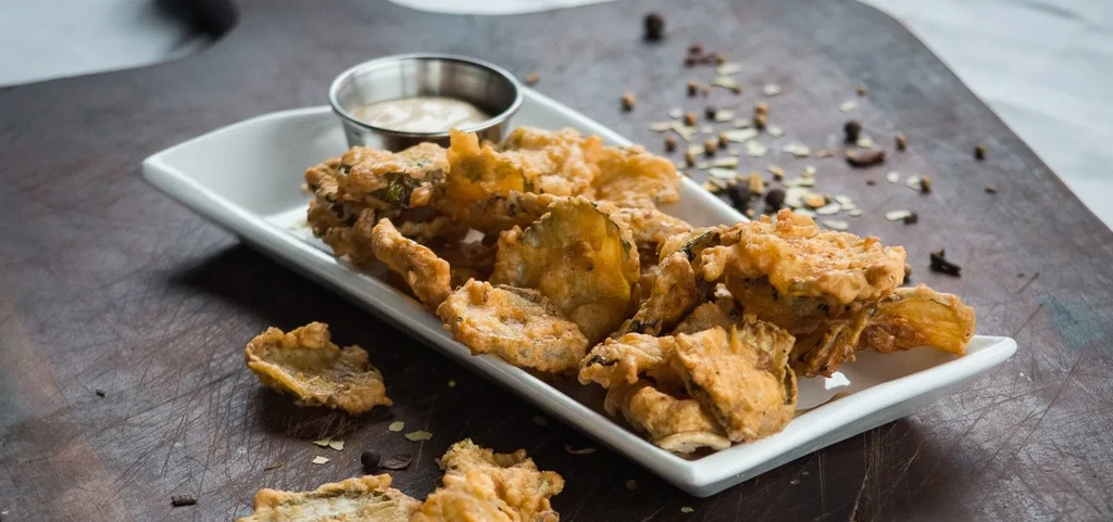 Crispy fried vegetable chips and dipping sauce on a white plate.