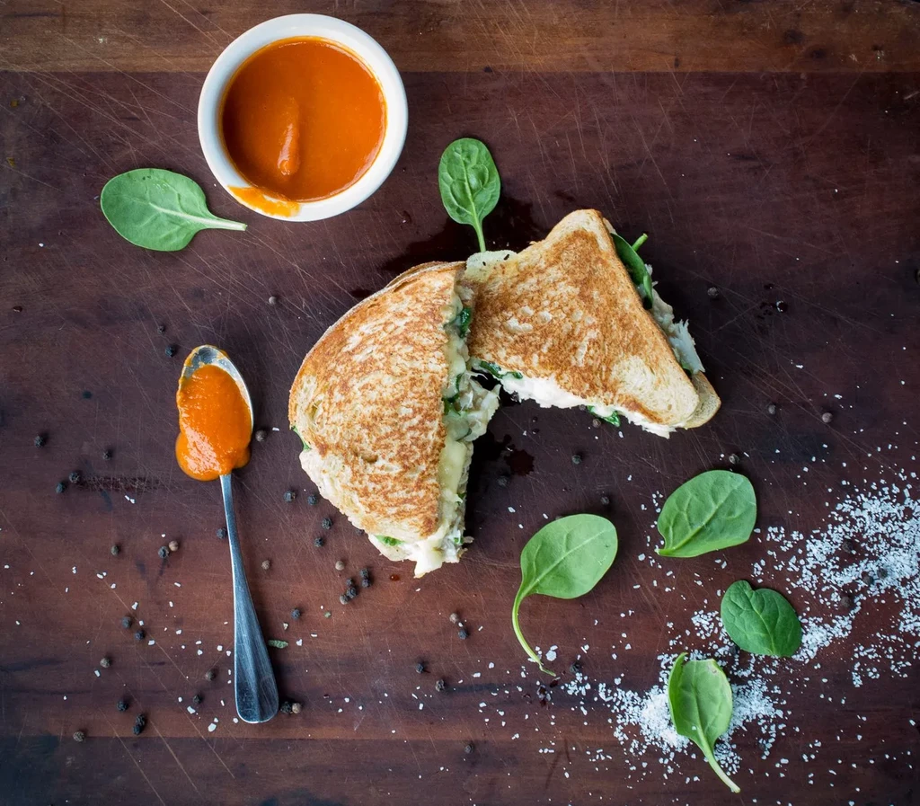 Overhead: Grilled cheese, tomato soup, spinach, peppercorns, salt on wood.