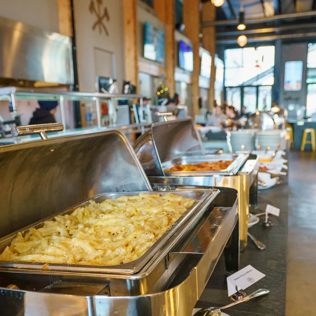 Two chafing dishes on a buffet, one labeled "Baked Penne Alfredo."
