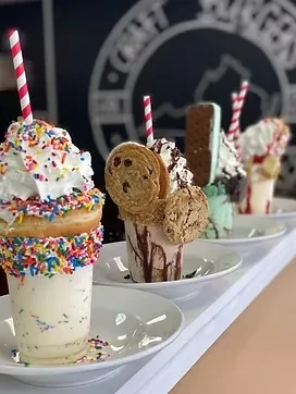 Four elaborately decorated milkshakes topped with donuts, cookies, and sprinkles.