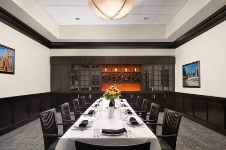 Elegantly set private dining room with long table and illuminated wine rack.