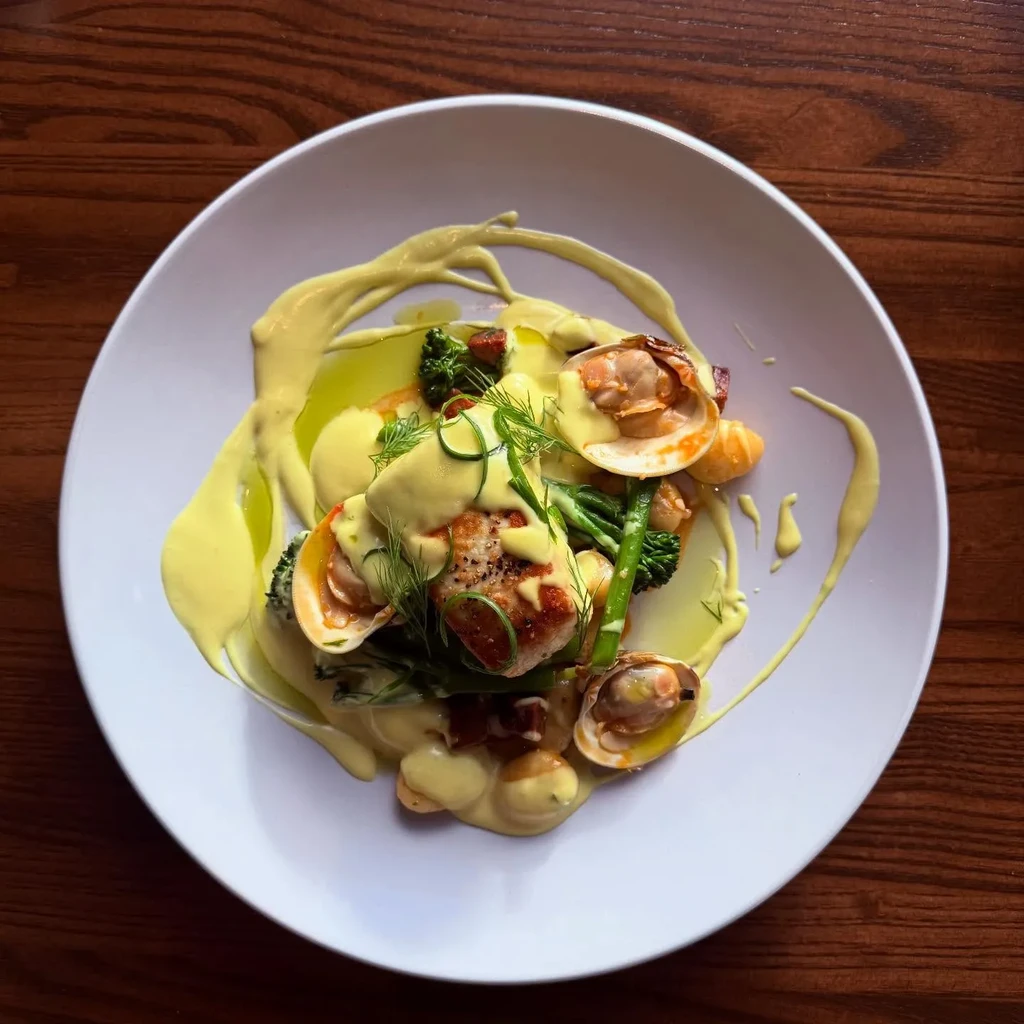 Gourmet seared fish and clam dish with vegetables and creamy sauce.