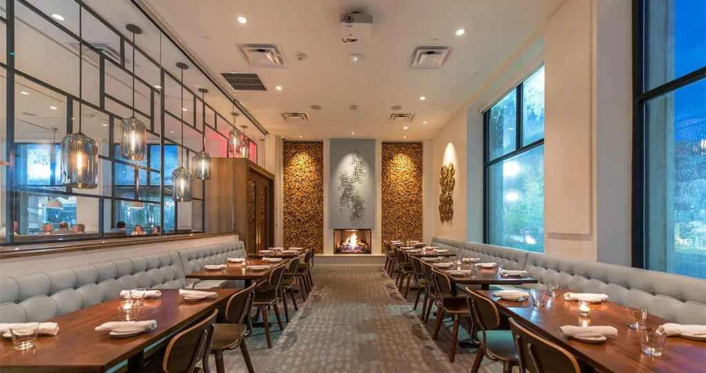 Modern dining room with set tables, fireplace, large windows, and banquettes.