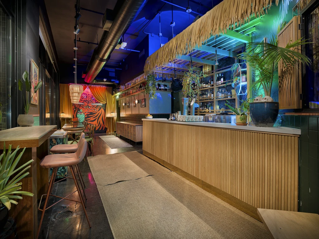 Vibrant, eclectic bar interior with tiger mural, thatched bar, and plants.
