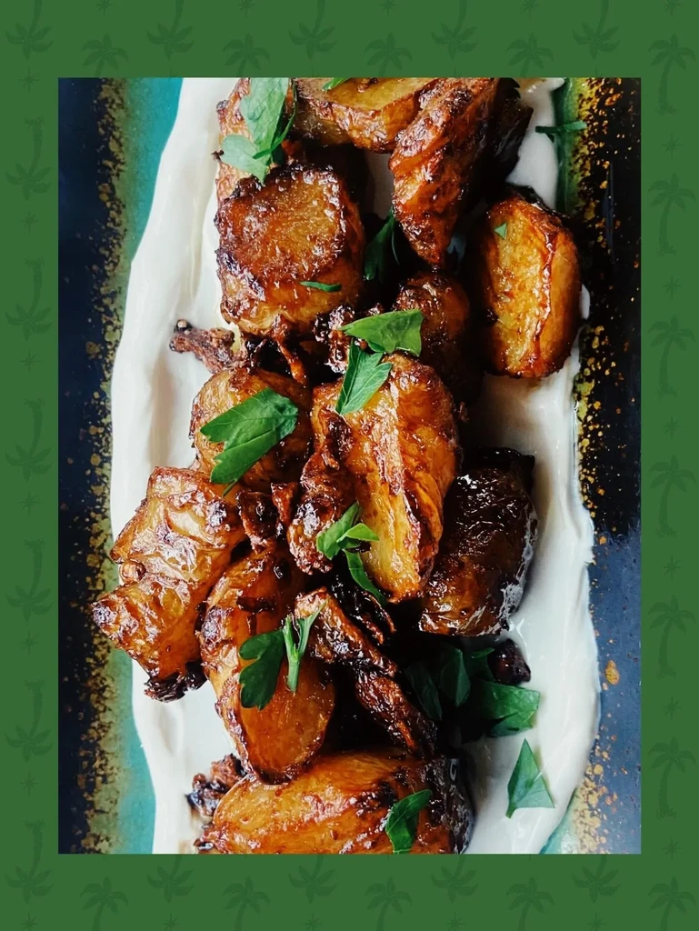 Glazed roasted potatoes with herbs atop creamy sauce, patterned plate.