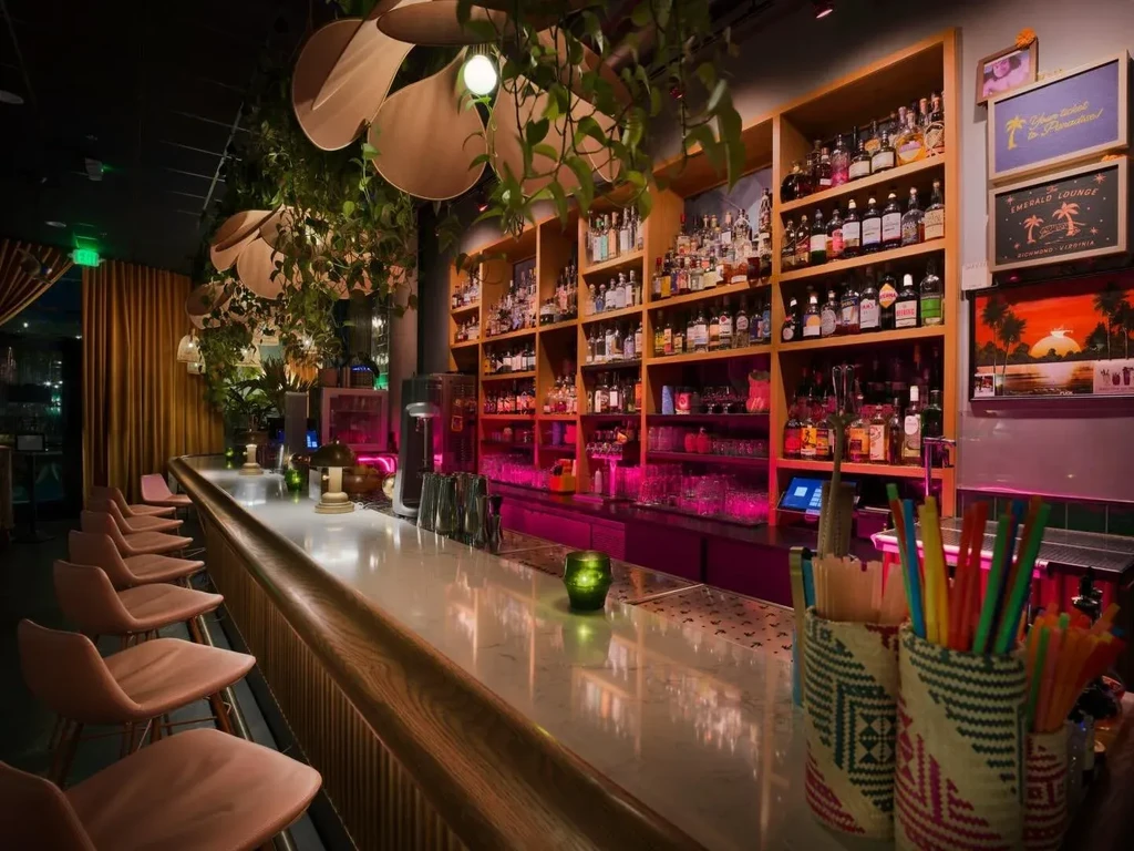 The Emerald Lounge bar: pink stools, tropical greenery, illuminated liquor bottles.