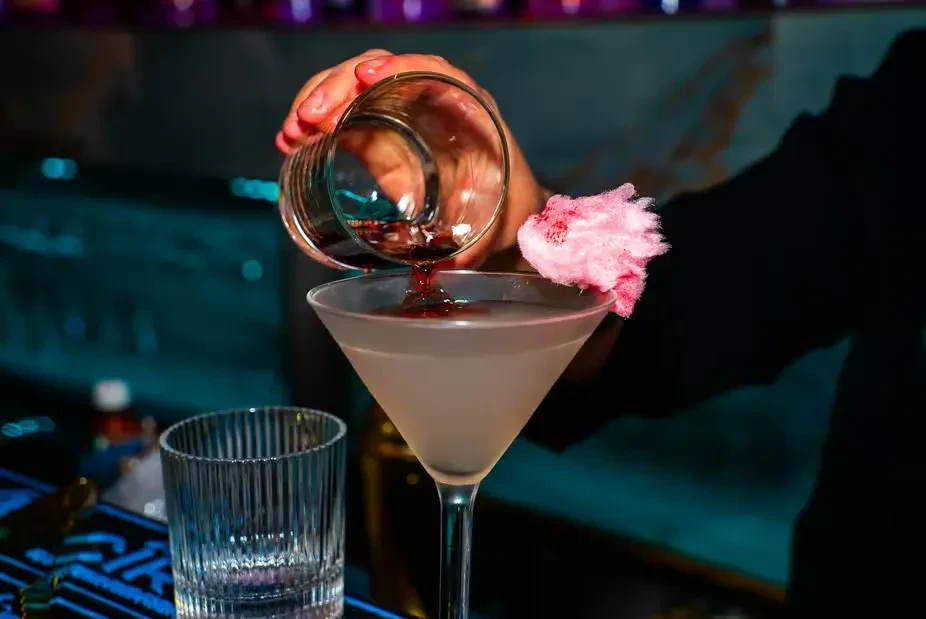 Bartender's hands pour a cocktail with pink cotton candy garnish.