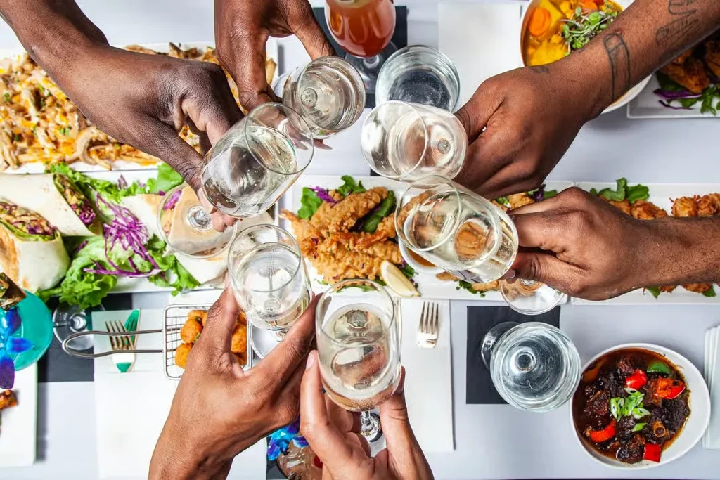 Multiple hands clinking glasses over a table of diverse dishes.