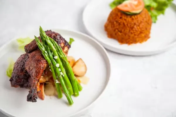 Two plates of roasted meat with asparagus and jollof rice.