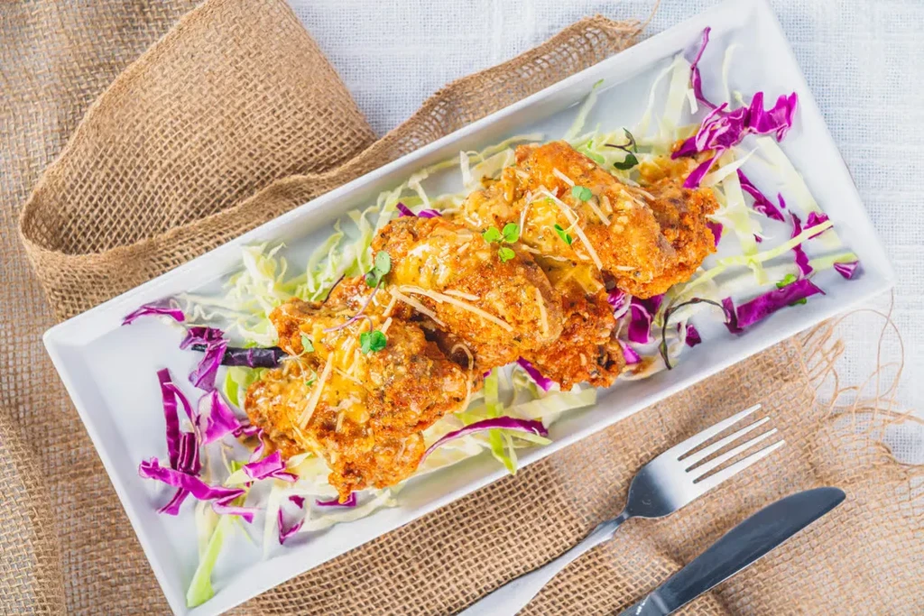 Golden fried food with creamy sauce, cheese, and herbs on colorful cabbage.