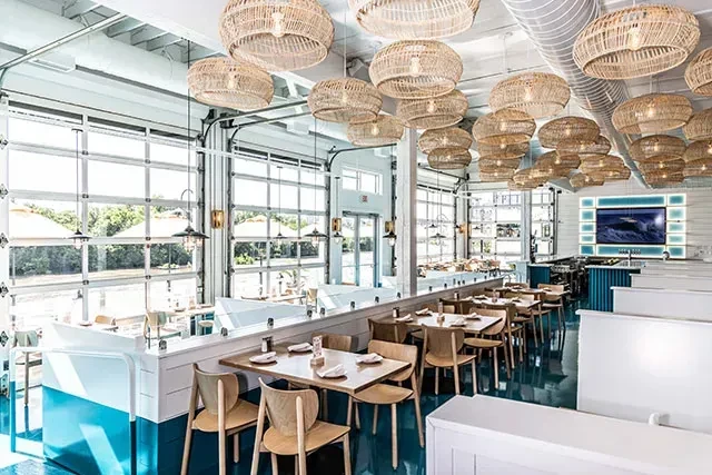 Bright, modern coastal restaurant interior with teal floor and wicker lighting.