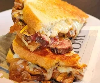 Stacked toasted sandwich with oozing cheese, meat, and caramelized onions.