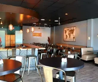 Modern restaurant interior with a bar, varied seating, and wooden world map art.