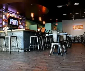 Empty modern restaurant with wooden bar, stools, and dining tables.